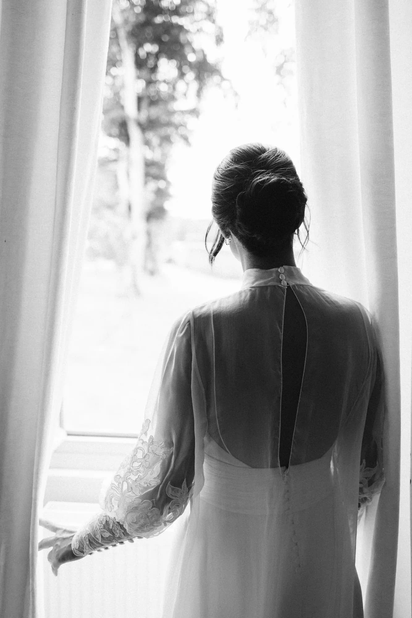 Mariée de dos devant une fenêtre, chignon et voile réalisés par Julia Trombetta